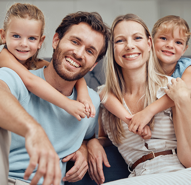Happy family of four smiling together indoors, showing warmth and dental health awareness.